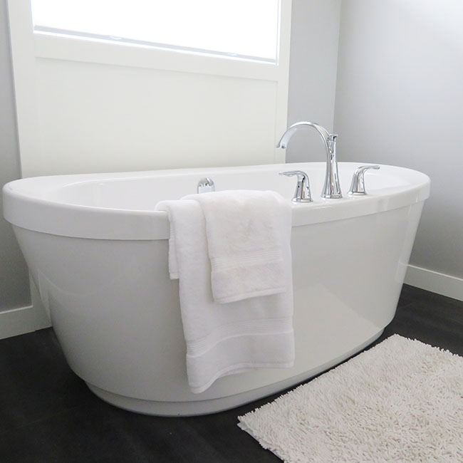 Freistehende Badewanne auf dunklem Boden mit weißem Handtuch